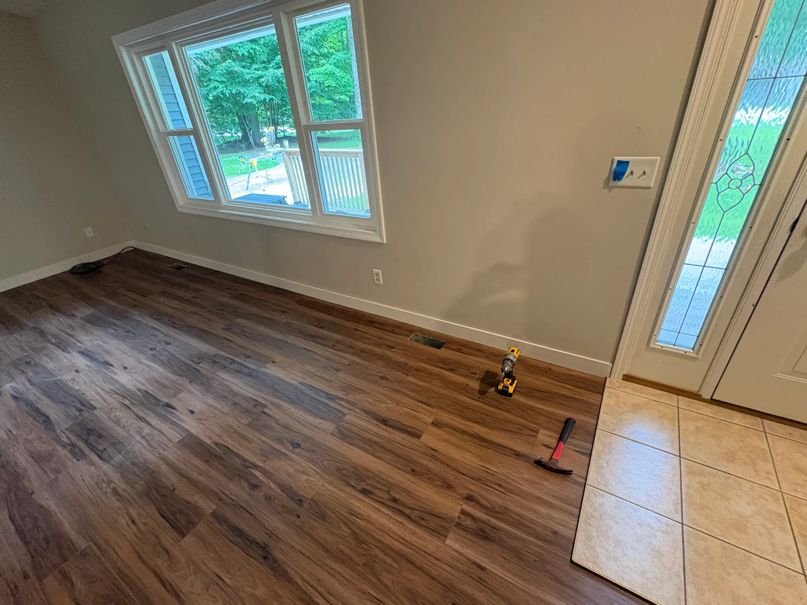 Walnut-tone luxury vinyl plank flooring installed beside beige ceramic tile at entryway with white baseboards