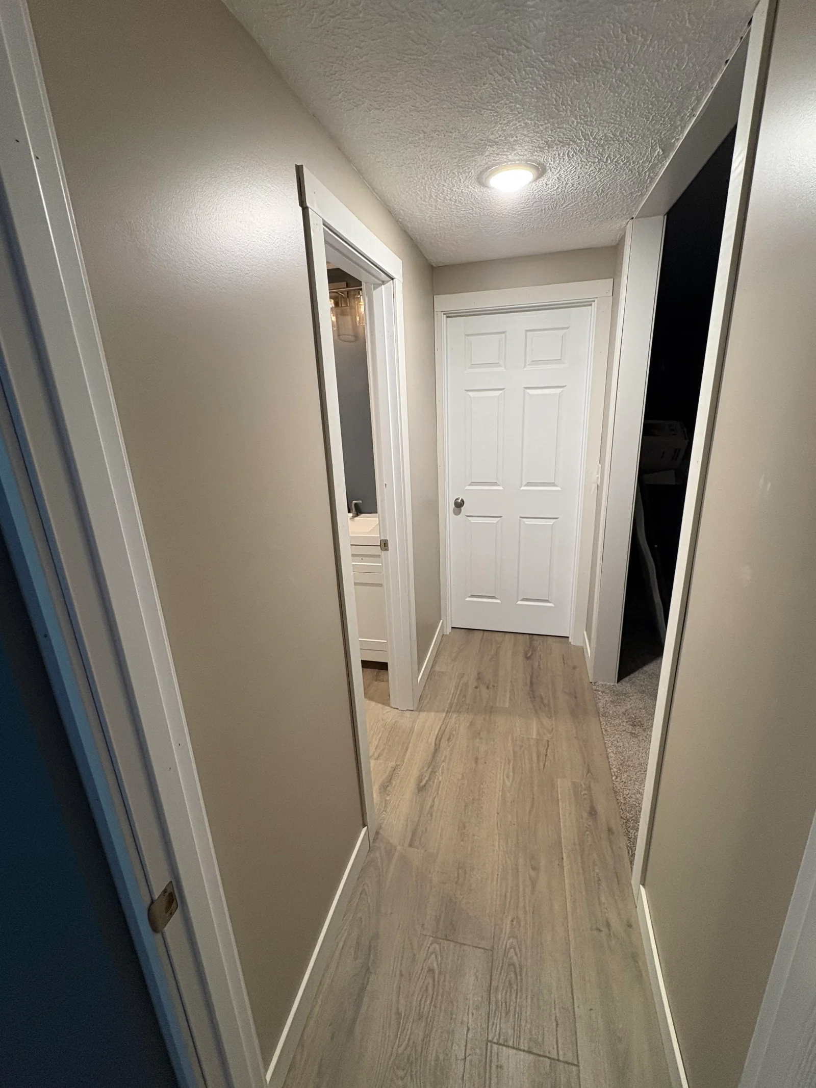 Narrow hallway with wood-look luxury vinyl plank flooring, white painted trim, greige walls, and textured ceiling