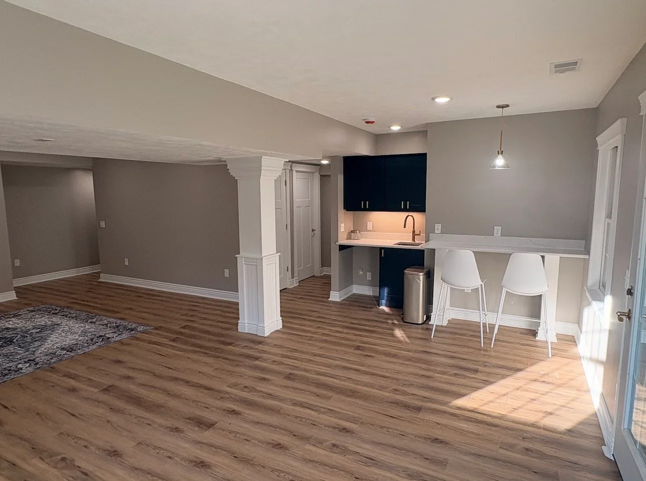 Finished basement with luxury vinyl plank floors, navy cabinets, quartz wet bar, and white breakfast bar