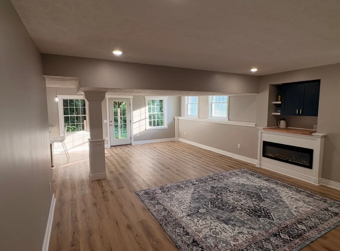 Finished basement living room with wood-look vinyl plank flooring, electric fireplace, navy built-in cabinets, and white trim