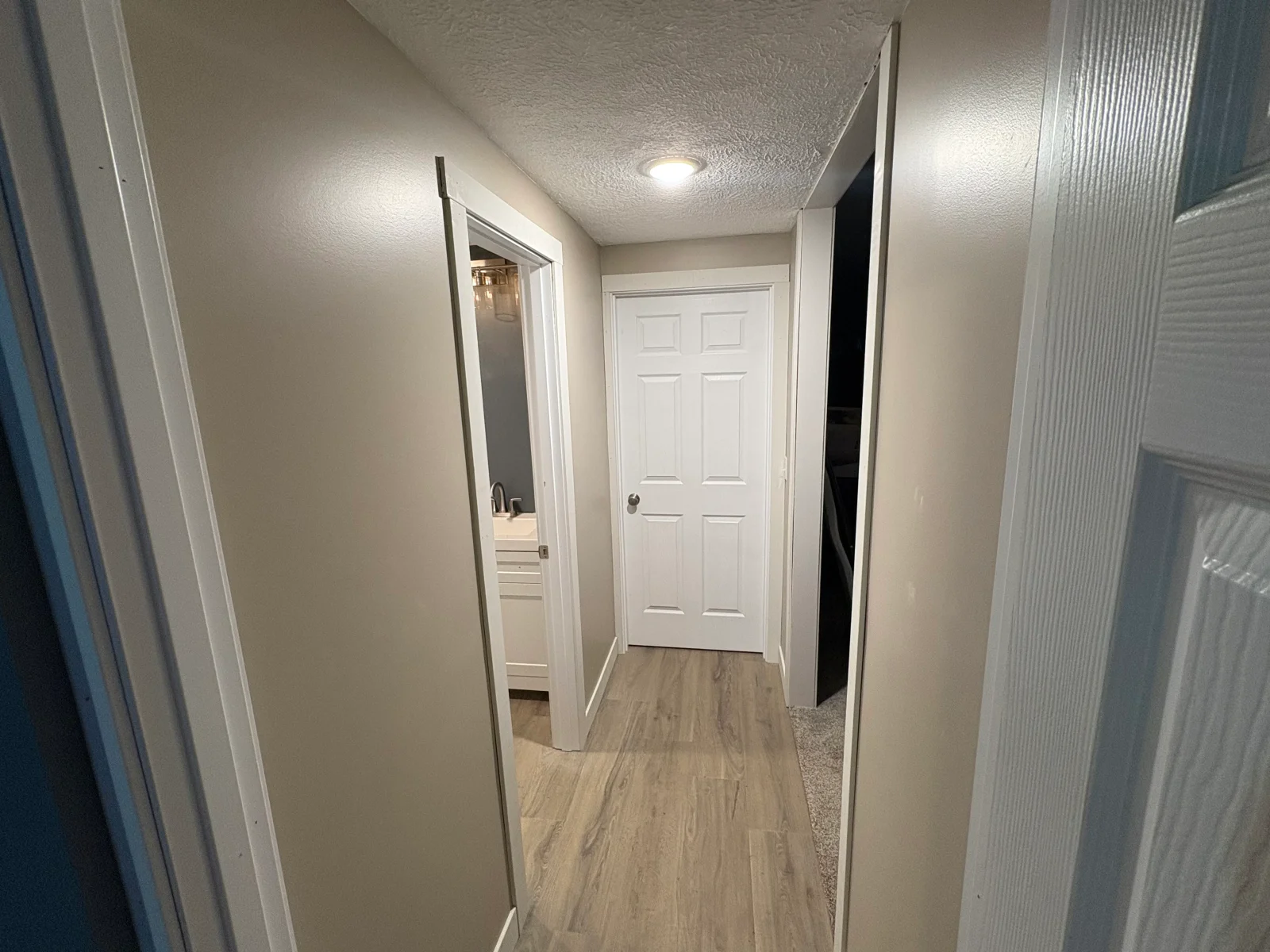 Hallway with light wood-look vinyl plank flooring, gray painted walls, white trim, and white six-panel doors