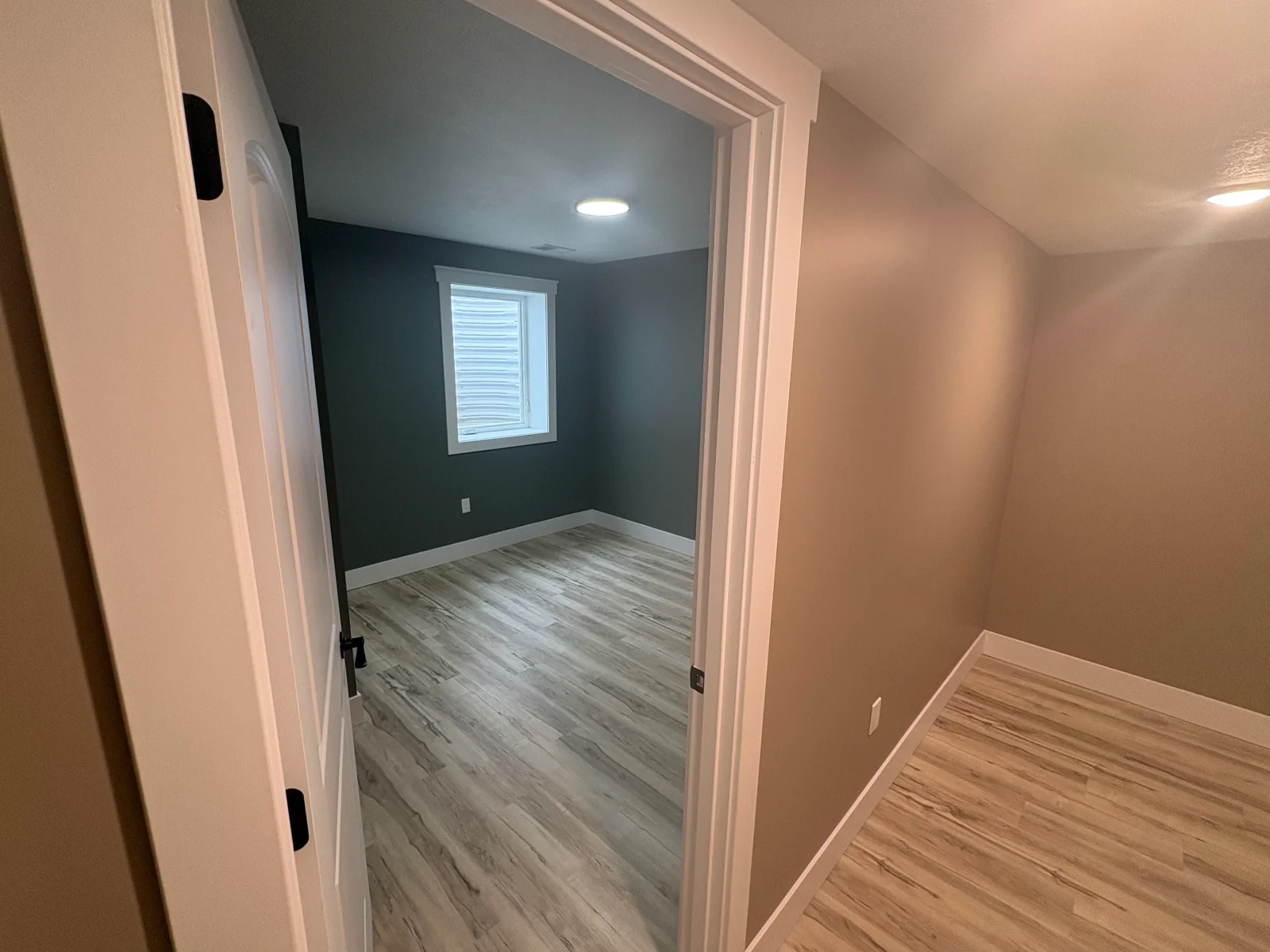 Finished bedroom with gray luxury vinyl plank floors, slate-green walls, white window trim, and taupe hallway with recessed lighting